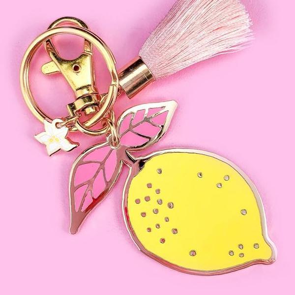 By Little Arrow. Lemon Keychain: Cloisonné hard enamel set in 22kt plated gold. Plated gold hardware and adorned with a silk tassel. Large lobster clasp. Illustrated by Brianna Bulski. Measures 3 x 2 inches. Also available in store at FOLD Gallery DTLA.