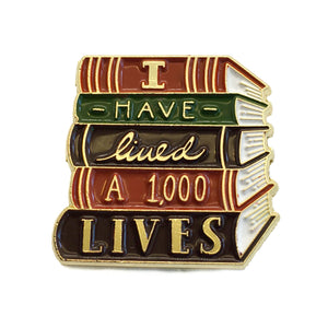 By Ectogasm. The I Have Lived 1,000 Lives Pin is a gorgeous enamel pin for book lovers. It features a stack of books with the quote, "I Have Lived 1,000 Lives". This durable pin is made with gold plated metal and enamel. It is kept secure with a metal clasp. Use it to show your love of reading with every outfit. Makes a charming gift for readers and librarians.  Measures 1" x 1"