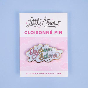 By Little Arrow. Iridescent glitter makes this Daydream Believer Pin totally magical. Cloisonné hard enamel set in 22kt plated gold with dual pins and rubber backs. Measures 2.25 x 1.125 inches.