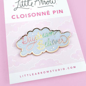 By Little Arrow. Iridescent glitter makes this Daydream Believer Pin totally magical. Cloisonné hard enamel set in 22kt plated gold with dual pins and rubber backs. Measures 2.25 x 1.125 inches.