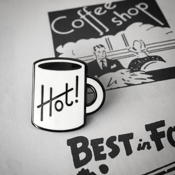 by Rather Keen. Have a hot cuppa! Hard enamel Hot Cuppa Pin. Black nickel metal with white enamel. Rubber clasp. Measures 7/8 inches tall. Also available in store at FOLD Gallery DTLA.