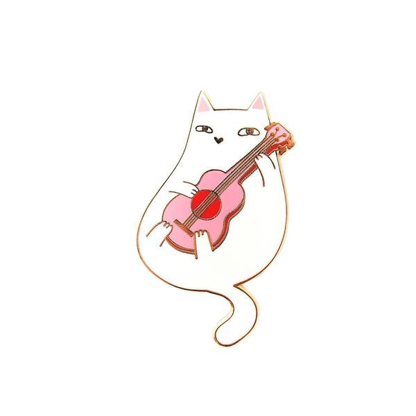 By Shoal. Ukulele Cat Pin. Hard enamel with shiny gold metal finish. Comes with double pin posts and two rubber clutch backs. Measures 1.6 inches tall. Also available in store at FOLD Gallery DTLA.