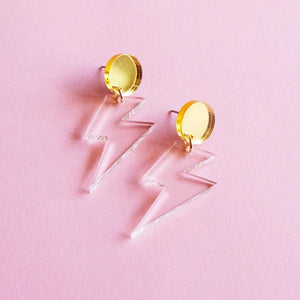 By Sleepy Mountain. Lightning Bolt Dangle Earrings: Gold studs with clear acrylic lightning bolt dangles. Light weight and comfortable. Mirror gold acrylic circle. Titanium stud attached to the back (Nickel-free, safe for sensitive ears). Clear acrylic. Measures overall size 2 inches. Bolt size 1.4 inches. Also available in store at FOLD Gallery DTLA.