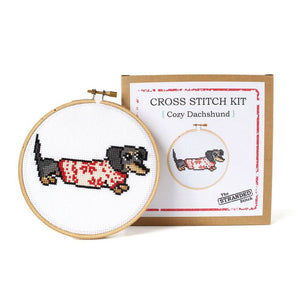 By The Stranded Stitch. Cozy Dachshund DIY Cross Stitch Kit Includes: Counted cross stitch pattern. Embroidery needle. Embroidery hoop. DMC embroidery thread. 14 count aida cloth. Step by step instructions. Box measures 6.25 x 1 x 6.25 inches. FOLD Gallery Dtla.