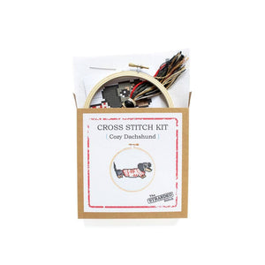 By The Stranded Stitch. Cozy Dachshund DIY Cross Stitch Kit Includes: Counted cross stitch pattern. Embroidery needle. Embroidery hoop. DMC embroidery thread. 14 count aida cloth. Step by step instructions. Box measures 6.25 x 1 x 6.25 inches. FOLD Gallery Dtla.