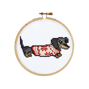 By The Stranded Stitch. Cozy Dachshund DIY Cross Stitch Kit Includes: Counted cross stitch pattern. Embroidery needle. Embroidery hoop. DMC embroidery thread. 14 count aida cloth. Step by step instructions. Box measures 6.25 x 1 x 6.25 inches. FOLD Gallery Dtla.